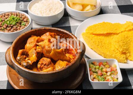 Pollo di Capoeira con couscous brasiliano, abbinato a riso, fagioli, manioca e vinaigrette, su un piatto bianco in cima a una linguetta a scacchi bianca e nera Foto Stock