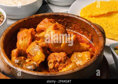 Pollo di Capoeira con couscous brasiliano, abbinato a riso, fagioli, manioca e vinaigrette, su un piatto bianco in cima a una linguetta a scacchi bianca e nera Foto Stock