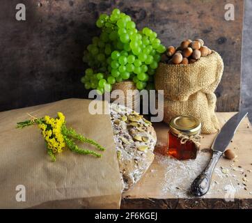 Pane rustico con un mazzo di uve, noci in sacchetto, miele, coltello. Foto Stock