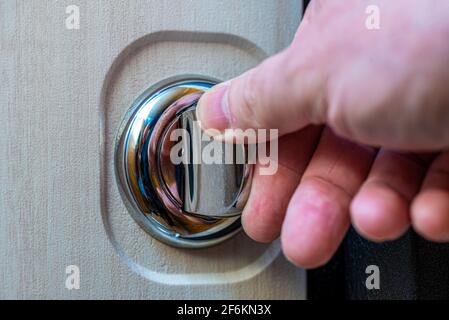 Primo piano di una mano umana su un dispositivo di chiusura rotondo dello sportello. Mobili per porte. Messa a fuoco selettiva. Mettere a fuoco il dispositivo di chiusura. Foto Stock