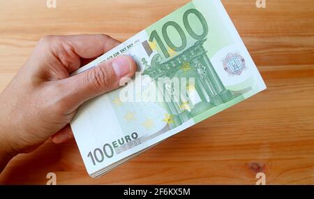 Manuale di tenuta pacchetto di 100 EURO banconote su legno Sfondo Foto Stock