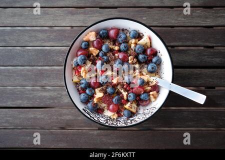 Ciotola di muesli allo yogurt (muesli) con frutti di bosco freschi e noci un tavolo di legno Foto Stock