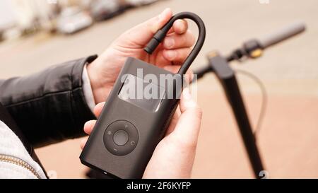 Un uomo pompa aria nella ruota di uno scooter elettrico utilizzando un dispositivo speciale. Foto Stock