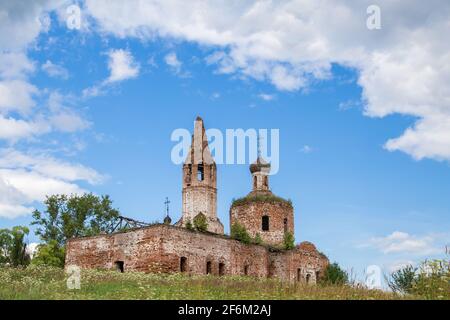 Antico cherkov distrutto contro il cielo blu. Il tempio in mattoni rossi si erge su una collina ricoperta di erba verde. Calda giornata estiva. Foto Stock