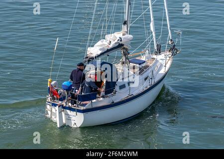 una coppia anziana o anziana si ritessa su un grande yacht a vela o barca che entra nel porto e nel porticciolo di lymington. Foto Stock