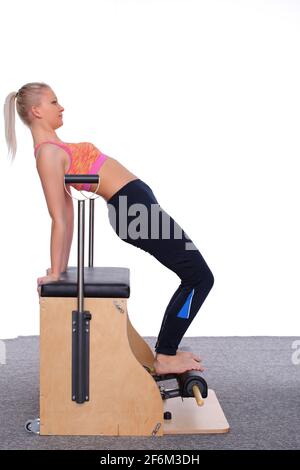 Un formatore di 20 anni fa pratica Pilates su una sedia dell'ascensore, piegandosi in una posizione del ponte. Foto Stock