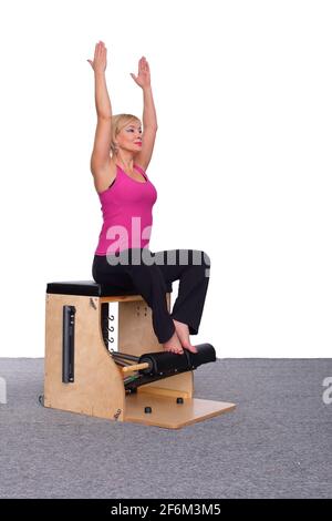 Un addestratore di 50-year-old pratica Pilates su una sedia dell'ascensore, sollevando le sue braccia in alto sopra la sua testa. Seduto Foto Stock