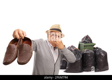 Uomo anziano che tiene un paio di scarpe stinky vicino a. contenitore e sacchetti per rifiuti isolati su sfondo bianco Foto Stock