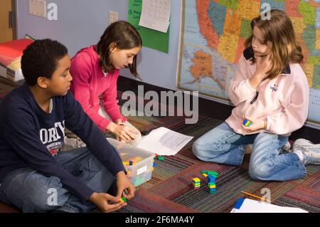 Scuola elementare indipendente grado 4 età 9-10 gruppo matematico di due ragazze ed un ragazzo che lavorano insieme i problemi usando la matematica manipolativi Foto Stock