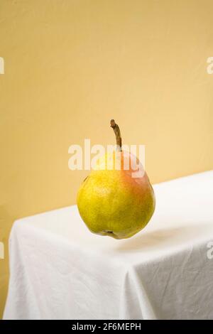 Pera che galleggia nell'aria su un tavolo bianco e sfondo giallo. Foto Stock