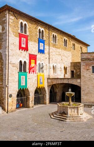 La piazza centrale della città medievale di Bevagna, Terni, Umbria, Italia, con la fontana e le bandiere dei quartieri per il palio Foto Stock