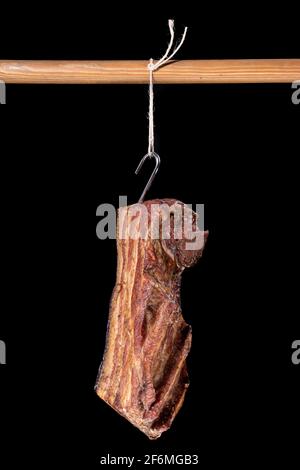 Deliziosa pancetta affumicata appesa su una corda. Carni preparate secondo la ricetta di casa. Sfondo scuro. Foto Stock