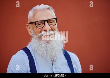 Allegro uomo hipster in atmosfera accogliente in posa sulla parete rossa Sfondo - persona alla moda in abiti casual moda - felice concetto di stile di vita anziano Foto Stock