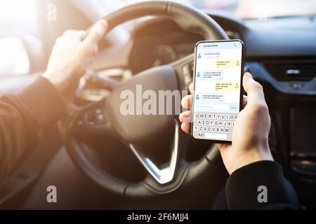 Uomo che digita un messaggio di testo sul telefono cellulare durante la guida dell'auto Foto Stock
