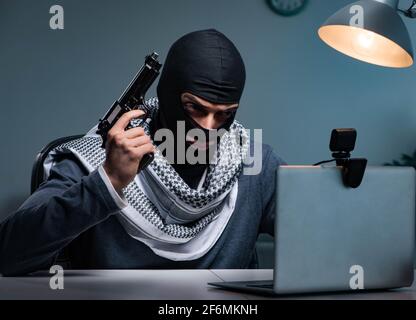 Il terrorista ladro con la pistola lavorando al computer Foto Stock