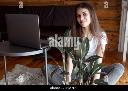 Pensivo ottimista femmina freelance studente in abito casual seduta su il pavimento e guardando la fotocamera Foto Stock