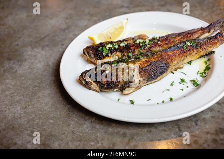 Due pesci di goda di mare fritti su piatto bianco con primo piano di limone. Cucina mediterranea, cibo spazzatura, gustosi spuntini per il concetto di birra Foto Stock