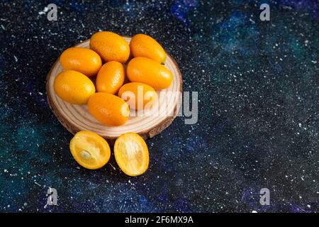 Primo piano foto di succosi kumquat su tavola di legno sopra sfondo blu Foto Stock