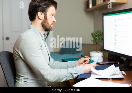 Uomo che lavora da casa su un computer desktop con documenti. HD 24 FPS. Foto Stock