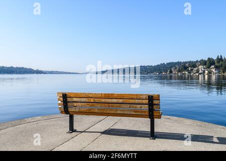 Una panchina sul bordo del lago Washington su un perfetto cielo blu mattina crea una sensazione di solitudine e. solitudine come guarda fuori su niente Foto Stock