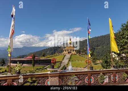 Statua di Buddha con fiori accanto alle bandiere di preghiera in primo piano a. Ravangla Sikkim India il 4 novembre 2016 Foto Stock