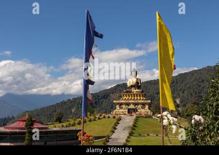 Statua di Buddha con fiori accanto alle bandiere di preghiera in primo piano a. Ravangla Sikkim India il 4 novembre 2016 Foto Stock