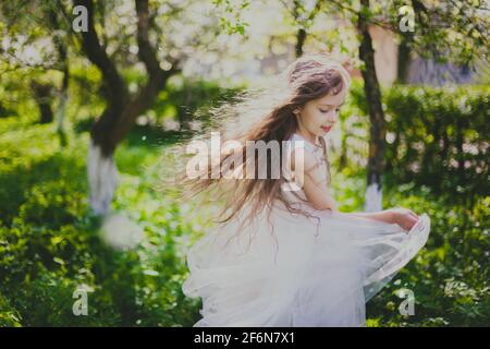 Bambina in giacca nera e abito bianco danzare il giardino di ciliegio primaverile Foto Stock