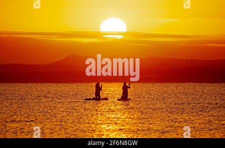 Portobello, Edimburgo, Scozia, tempo britannico. 2 aprile 2021. Buon sole per l'alba del Venerdì Santo, temperatura meno 1 gradi centigradi al mare sul Firth of Forth per i nuotatori di acqua fredda e duri e paddle Boarders. Foto Stock