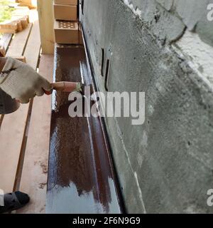 Un uomo dipinge un angolo di metallo con vernice marrone, lavorando su un cantiere site.New Foto Stock