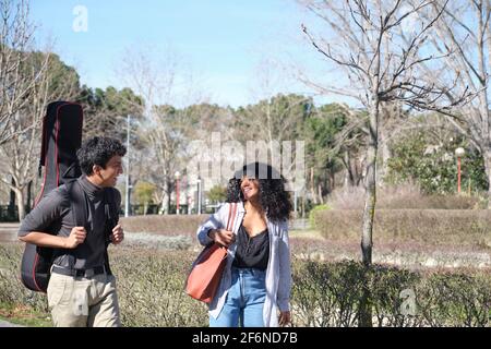 Amici latini che camminano per il campus universitario con una custodia per chitarra. Vita universitaria. Foto Stock