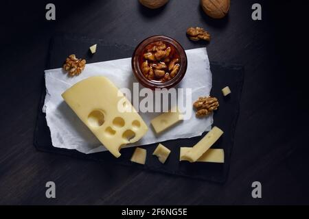 il formaggio tagliato a fette giace su un piatto di pietra con miele e noce su sfondo scuro. Vista dall'alto Foto Stock