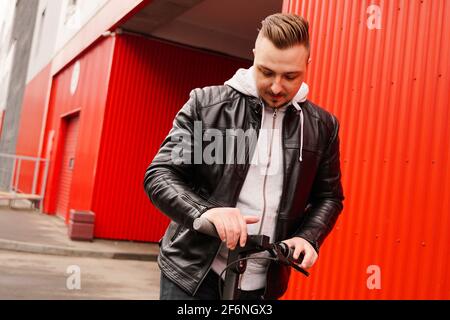 Giovane uomo attraente su scooter elettrico su sfondo rosso Foto Stock