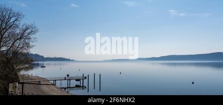 vista panoramica di un molo che conduce in una calma lago blu con foresta e colline sullo sfondo Foto Stock