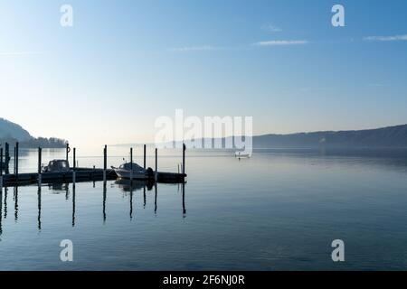 Una vista su un tranquillo lago blu con navi ormeggiate e un piccolo motoscafo che naviga attraverso l'acqua Foto Stock