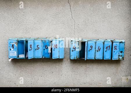 Vecchie caselle postali arrugginite sulla parete. Caselle di posta blu con numeri danneggiati. Alcune scatole sono aperte. Foto Stock