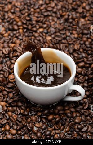 tazza bianca con spruzzi di caffè preparato su chicchi marroni Foto Stock