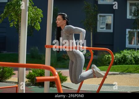 La giovane donna entra per lo sport sul terreno sportivo, esegue push-up sulle barre irregolari. Vista laterale. Foto Stock