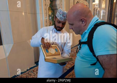 Un dipendente della moschea mostra una pagina splendidamente decorata del Corano ad un turista nella Grande Moschea del Sultano Qaboos, Mascate, Oman Foto Stock