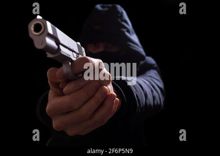 Uomo con pistola e nel cappuccio puntato con una gomma da vicino, isolato su un nero. Foto Stock