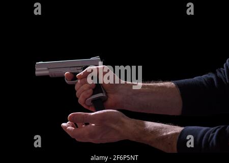 Mani maschili ricaricando caricatore pistola, isolato su sfondo nero. Foto Stock