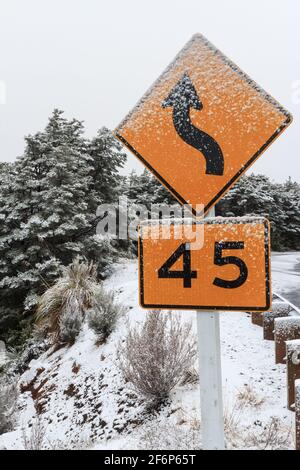 Una strada tortuosa e un segnale limite di velocità di 45 kp/h su una montagna innevata. Monte Ruapehu, Nuova Zelanda Foto Stock