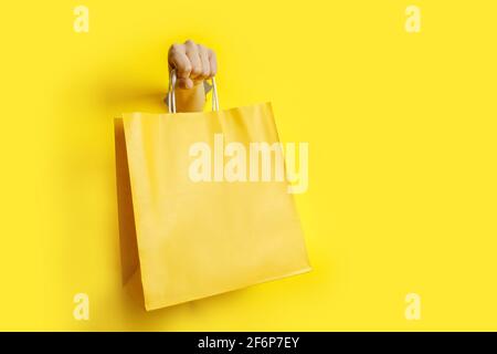 Donna mano che tiene il sacchetto di carta giallo su sfondo giallo Foto Stock