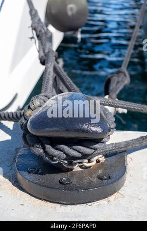 Concetto di paletto per ormeggio. Funi intrecciate con manopole su bullard in acciaio metallico nero. Yacht ormeggiati al porto di Floisvou, Grecia. Verti Foto Stock