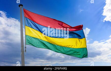 Bandiera di Mauritius, simbolo nazionale della Repubblica di Mauritius su un flagpole che oscilla contro il cielo blu nuvoloso Foto Stock