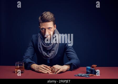 Elegante uomo bearded che gioca nel casinò scuro, fumare sigaro, bere whiskey Foto Stock