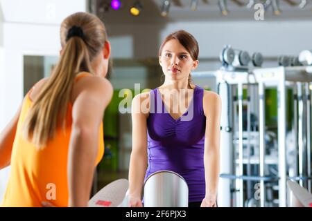 Due donne in palestra davanti a una macchina per esercizi avere una chat Foto Stock