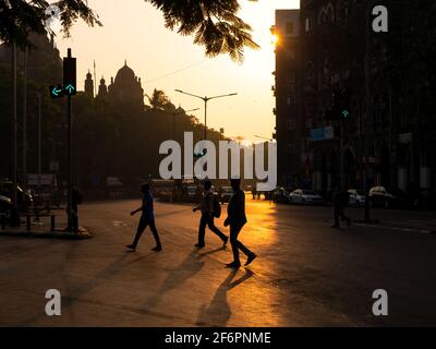 Mumbai, India - 7 gennaio 2021: Silhouette di persone che attraversano le strade con il sole che sorge in background e segnale di traffico in verde sulle strade di Foto Stock