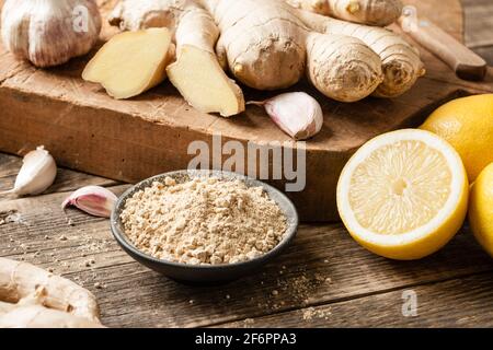 Radice di zenzero, polvere di zenzero, aglio e limoni freschi su tavola di legno Foto Stock