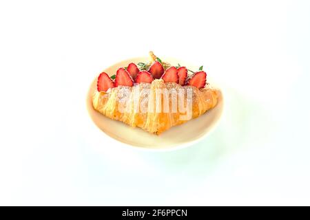 Croissant appena sfornato ripieno di fragole fresche su piatto bianco. Panino di croissant con fragole, isolato fatto in casa con fondo bianco. Foto Stock