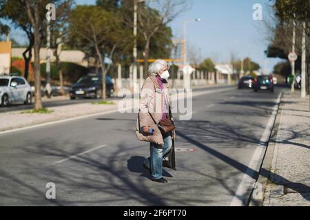 10 marzo 2021 - Faro, Portogallo: Donna anziana che indossa la maschera facciale che attraversa la strada Foto Stock